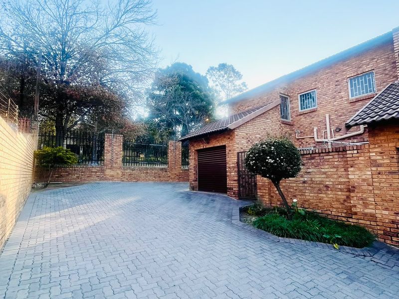 A well-maintained brick exterior featuring a paved driveway, secure perimeter fencing, and a private garage entrance.