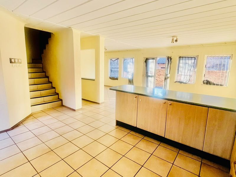 Spacious open-plan area featuring tiled flooring, built-in kitchen cabinetry with laminate countertops, and a staircase leading to the upper level.