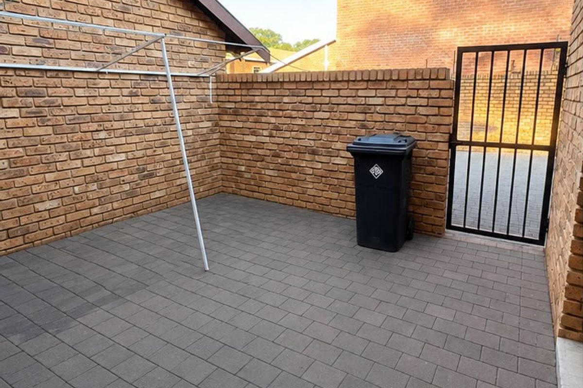 A private paved rear courtyard featuring brick boundary walls, a secure metal gate, and a wall-mounted clothesline.