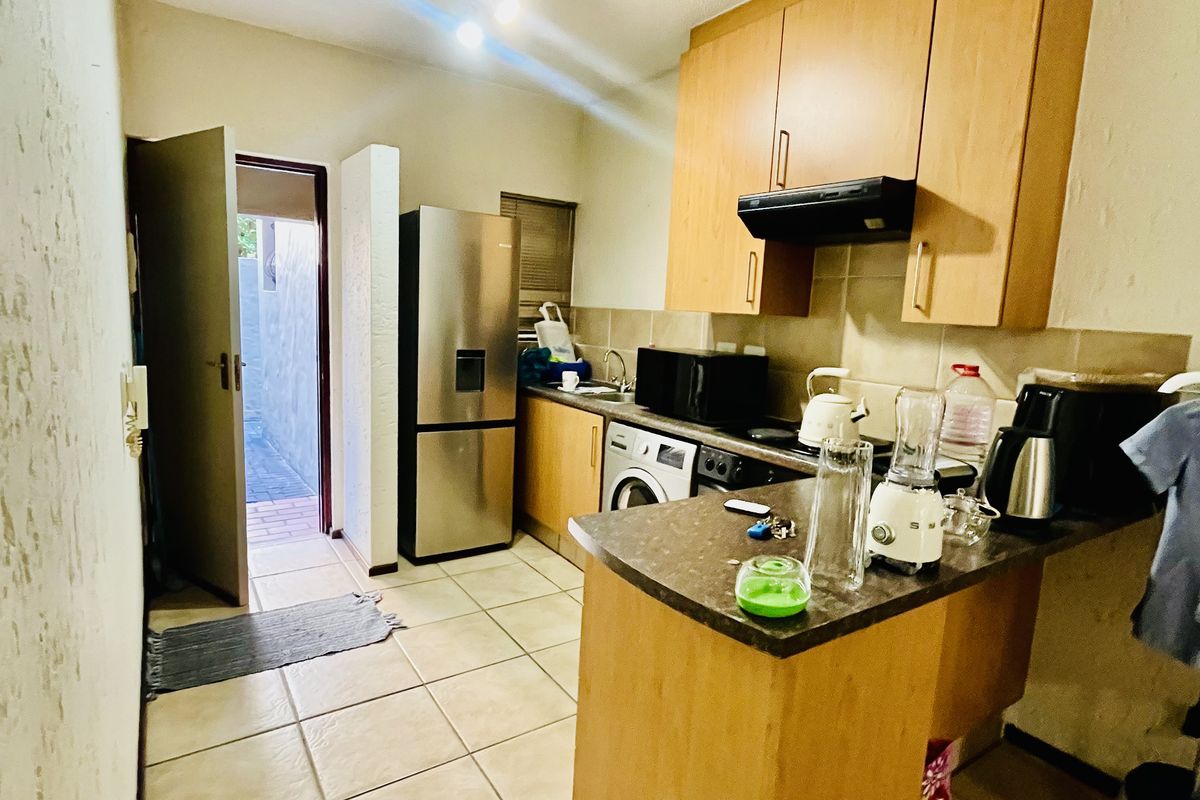 Compact kitchen featuring wooden cabinetry, laminate countertops, tiled flooring, and a tiled backsplash, with direct access to an exterior area.