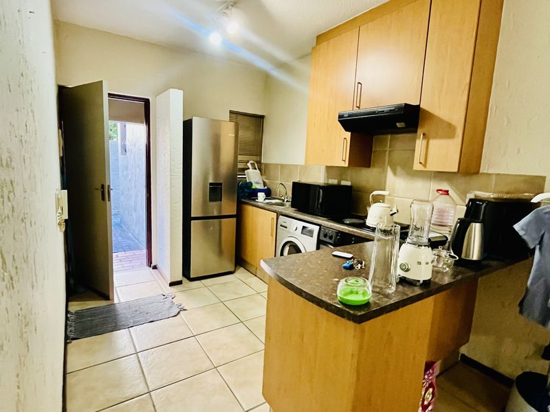 Compact kitchen featuring wooden cabinetry, laminate countertops, tiled flooring, and a tiled backsplash, with direct access to an exterior area.