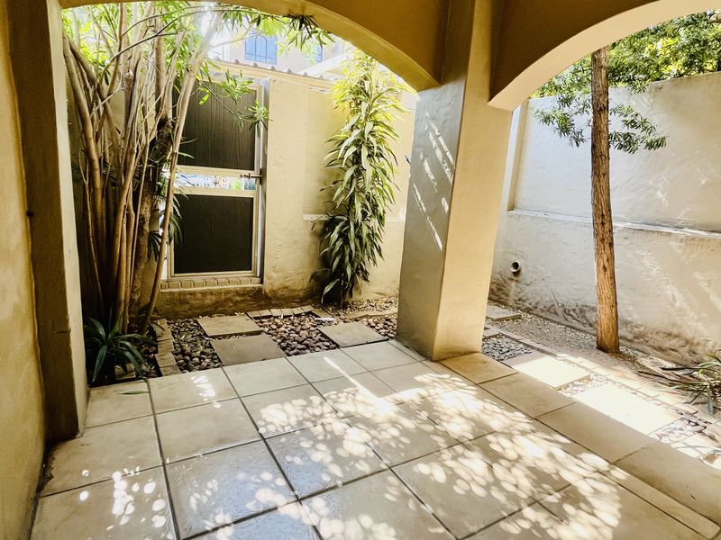 A covered patio area featuring tiled flooring, arched structural columns, and a small private courtyard space with a security gate.