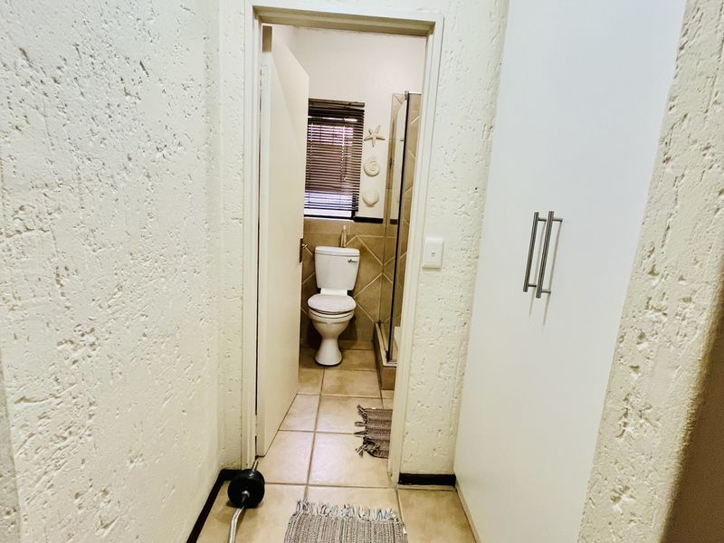 A hallway featuring textured walls and built-in cupboards, leading directly into a bathroom with tiled flooring.