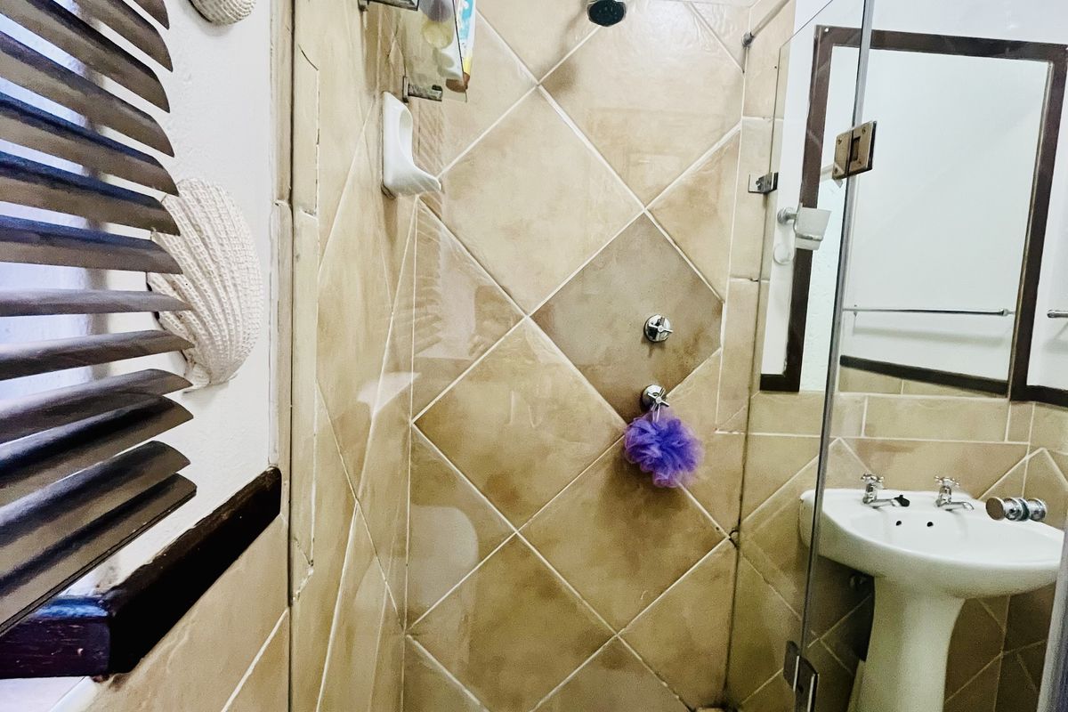 A compact bathroom featuring a glass-enclosed shower with diamond-patterned wall tiles, a pedestal basin, and a wall mirror.