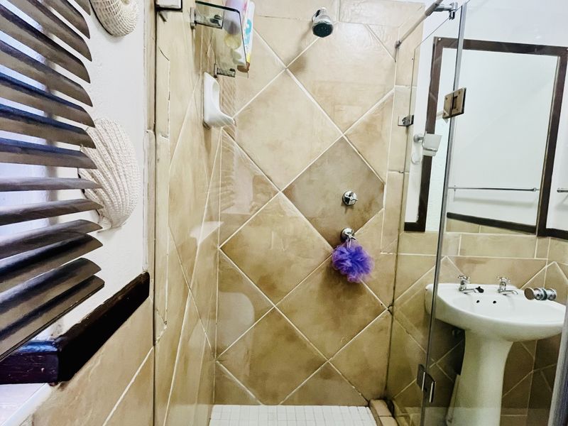 A compact bathroom featuring a glass-enclosed shower with diamond-patterned wall tiles, a pedestal basin, and a wall mirror.