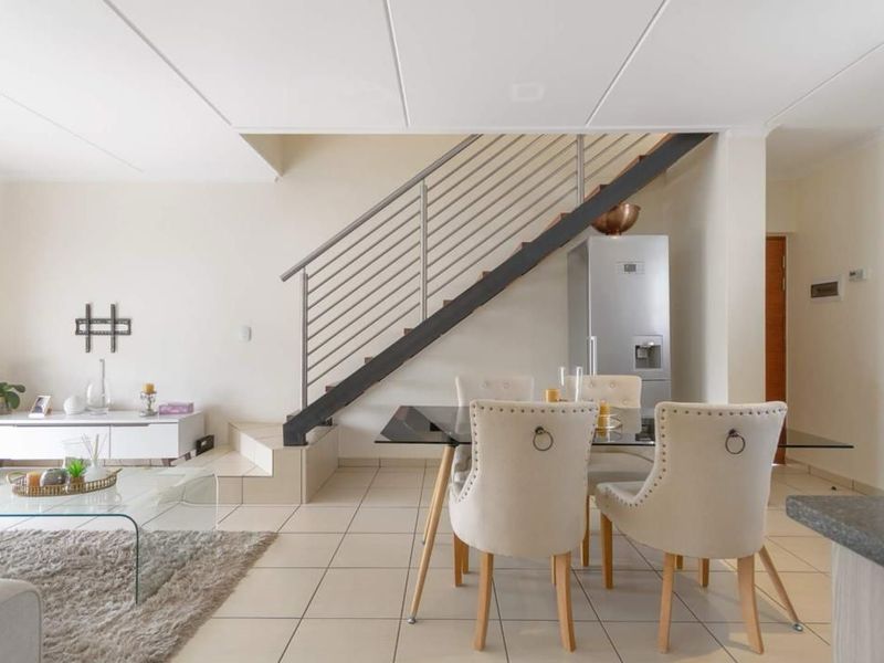 Open-plan living and dining area featuring tiled flooring, a modern staircase with metal balustrade, and a clean, neutral interior design.
