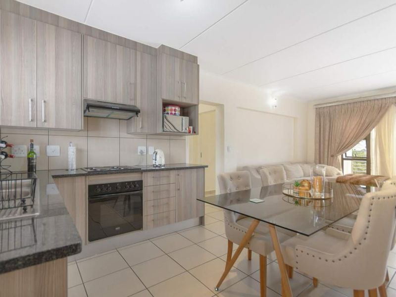 Open-plan living area featuring a modern kitchen with wood-finish cabinetry, granite countertops, built-in oven, and hob, flowing into a dining and lounge space.