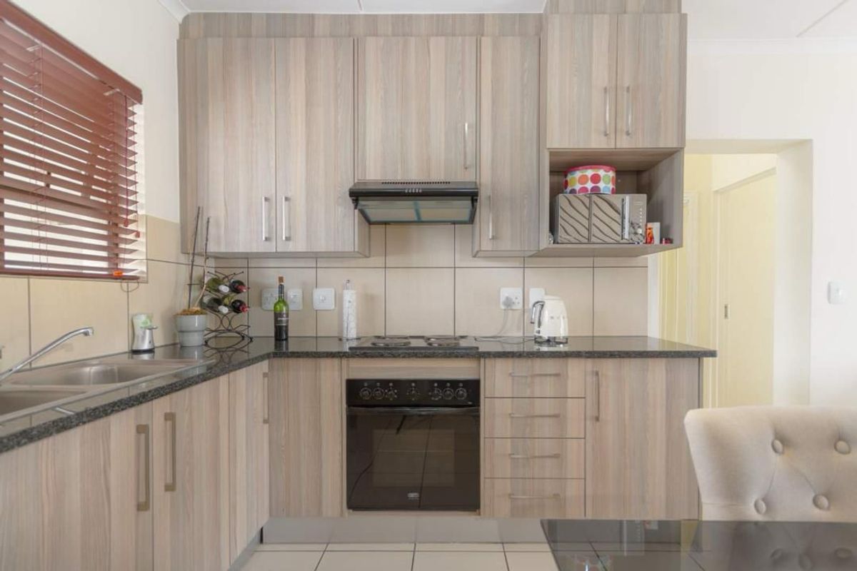 A functional kitchen featuring light wood-grain laminate cabinetry, granite countertops, a built-in oven with electric hob, and a tiled backsplash.