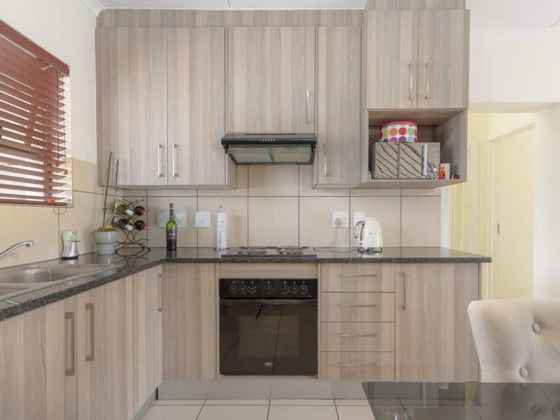 A functional kitchen featuring light wood-grain laminate cabinetry, granite countertops, a built-in oven with electric hob, and a tiled backsplash.