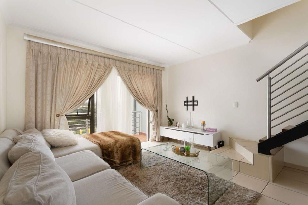A bright living room featuring tiled flooring, a staircase with a modern metal balustrade, and a sliding glass door leading to an outdoor area.