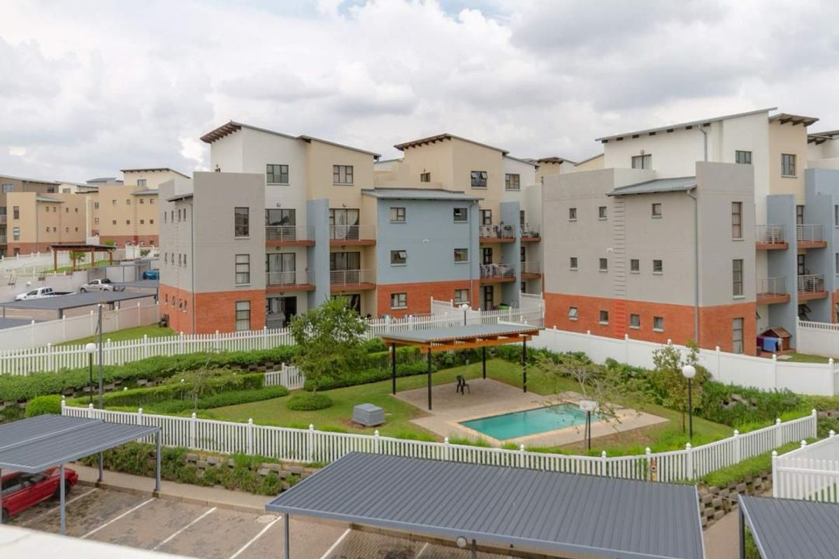 Aerial view of an apartment complex featuring a communal swimming pool, pergola, landscaped gardens, and covered parking bays.