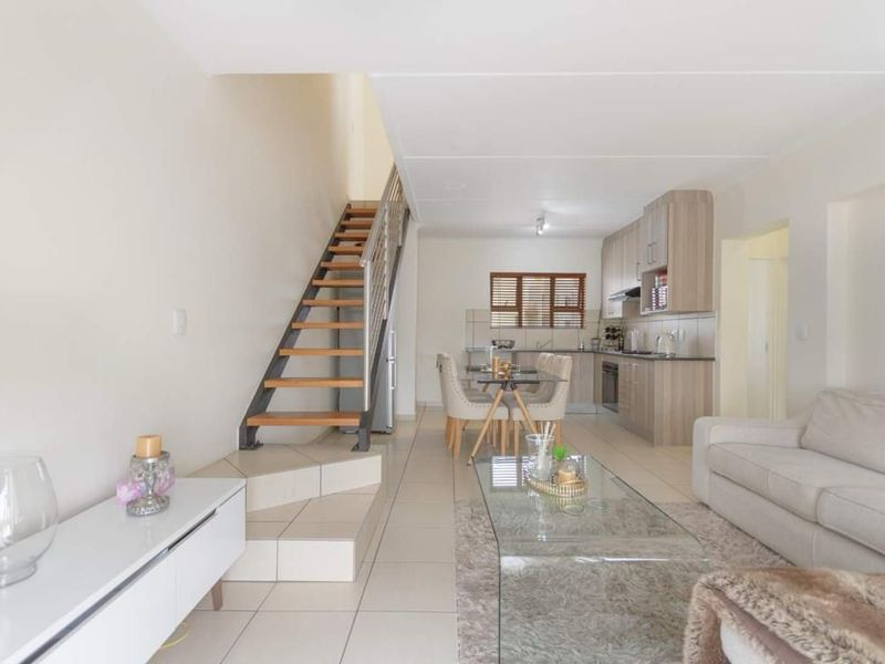Open-plan living and kitchen area featuring a modern staircase, neutral tiled flooring, and functional kitchen cabinetry with integrated appliances.