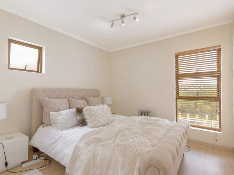 A well-lit bedroom featuring laminate flooring, built-in cupboards, and wooden venetian blinds, offering a clean and neutral living space.