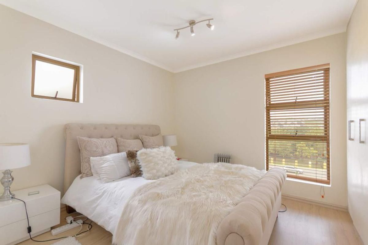 A well-lit bedroom featuring laminate flooring, built-in cupboards, and wooden venetian blinds, offering a clean and neutral living space.