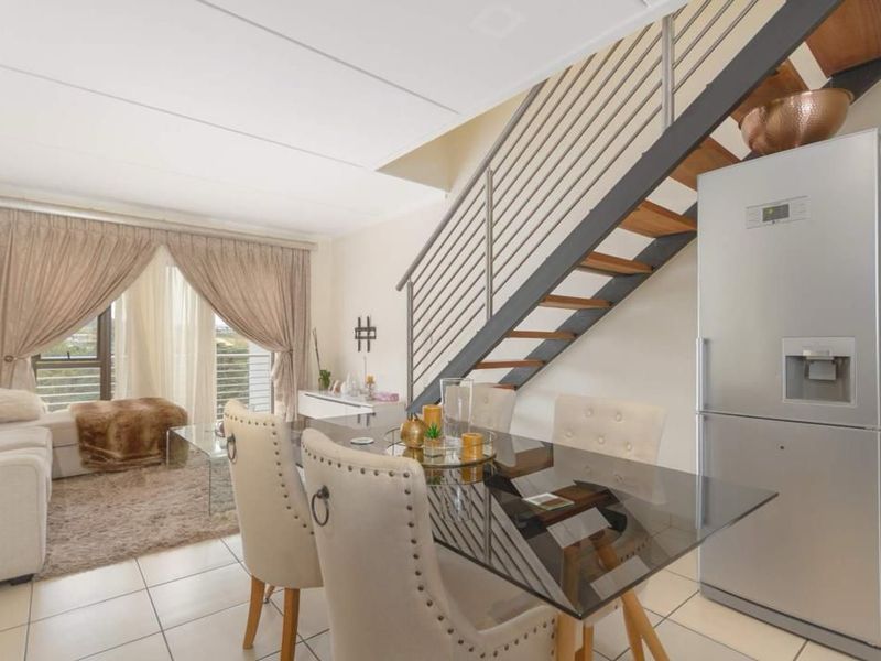 Open plan living and dining area featuring tiled floors, a modern staircase with metal balustrades, and access to a balcony through sliding glass doors.