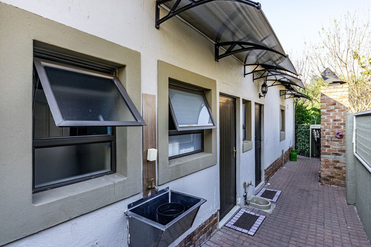 Rear exterior view showing a paved walkway, external utility sink, brick chimney, and multiple top-hung windows protected by polycarbonate awnings.