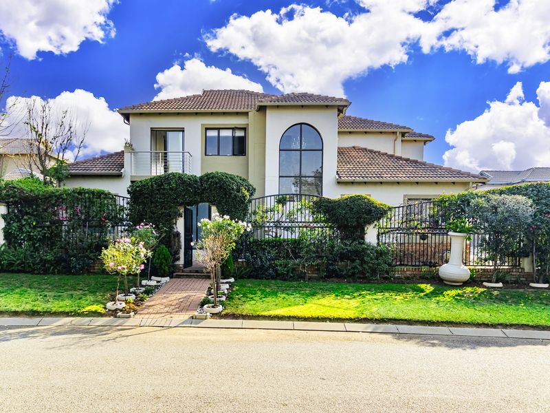 A well-maintained double-story residential property featuring a tiled roof, arched window, balcony, and a landscaped front garden with secure perimeter fencing.