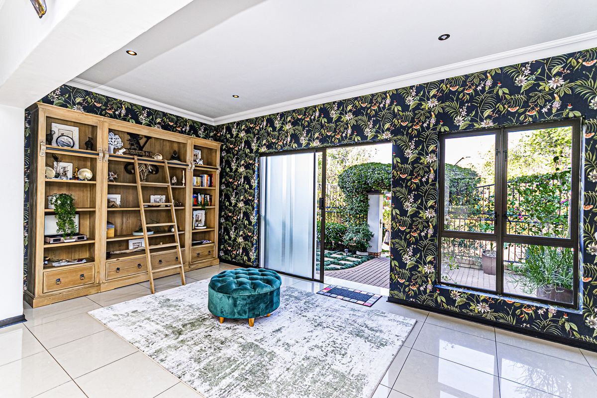 A bright living room featuring a large built-in wooden library unit, tiled floors, and direct access to the garden through a sliding glass door.