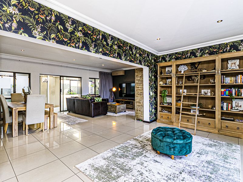 Spacious open-plan living and dining area featuring large-format floor tiles, recessed lighting, and a prominent built-in wooden library shelving unit.