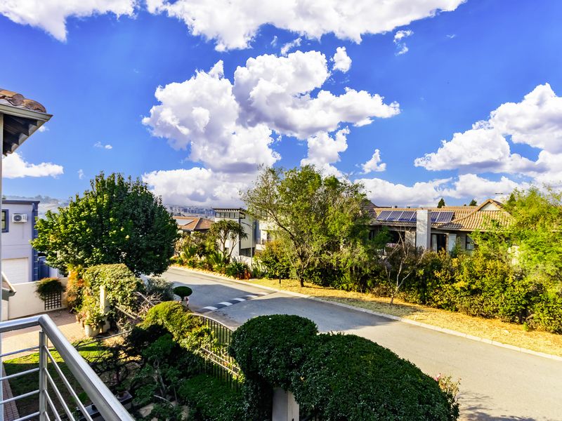 Elevated view overlooking a suburban street, featuring mature landscaping, residential rooftops, and clear blue skies.