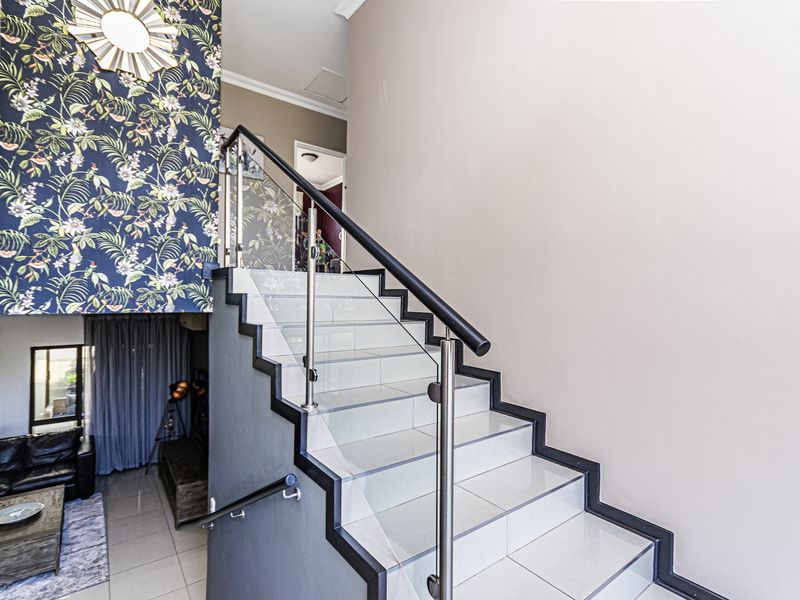 A modern staircase featuring tiled steps, a sleek glass balustrade with a metal handrail, and a striking floral feature wall.