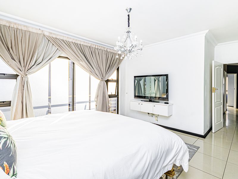 Spacious bedroom featuring polished tile flooring, crown molding, a crystal chandelier, and direct access to an outdoor area through sliding glass doors.