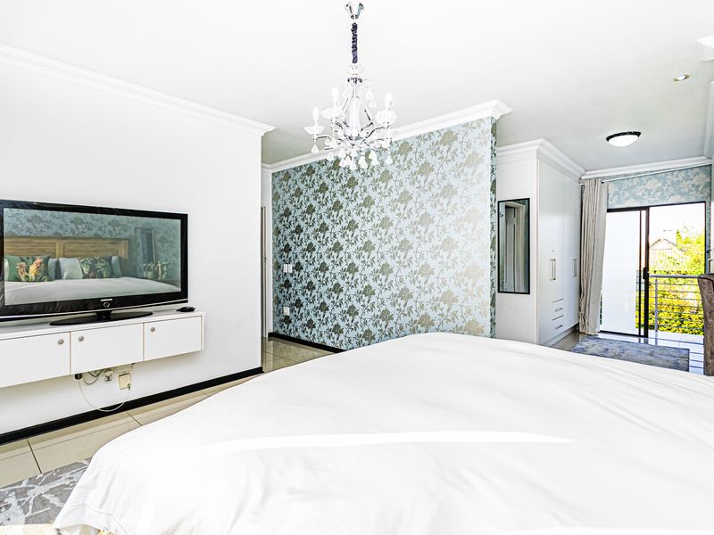 Spacious bedroom featuring built-in cupboards, decorative wallpaper, tiled flooring, and direct access to a private balcony through sliding glass doors.