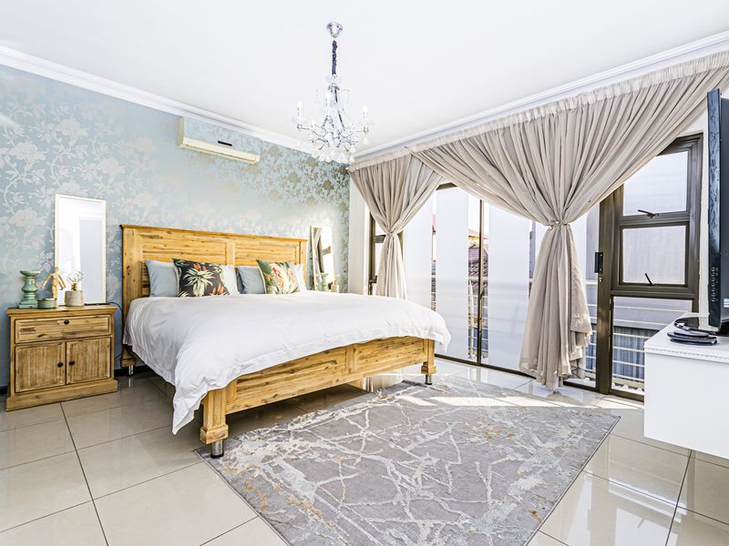 Spacious bedroom featuring tiled flooring, decorative wallpaper, a crystal chandelier, and direct access to a balcony through sliding glass doors.