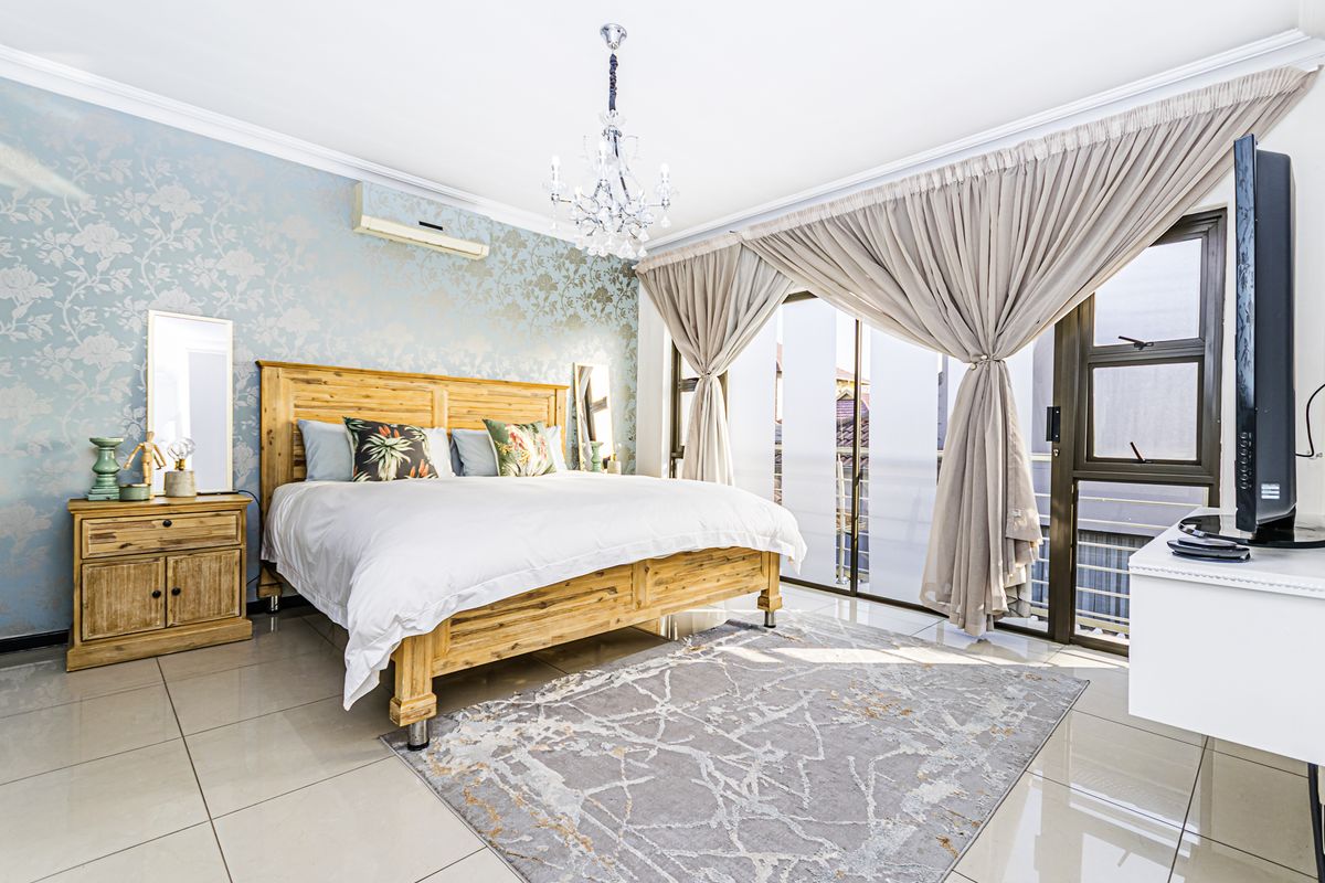 Spacious bedroom featuring tiled flooring, decorative wallpaper, a crystal chandelier, and direct access to a balcony through sliding glass doors.