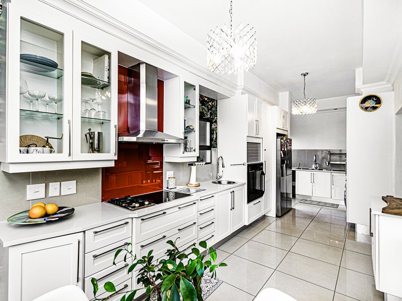 Modern kitchen featuring white cabinetry, stone countertops, a striking red glass splashback, built-in appliances, and tiled flooring, with an adjacent scullery area.