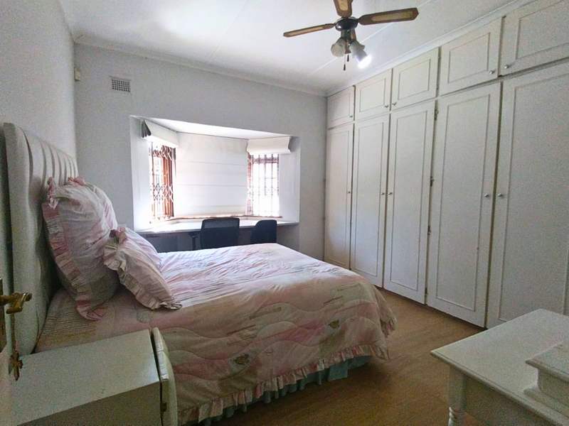Spacious bedroom featuring extensive built-in cabinetry, a dedicated built-in desk area within a bay window, and a ceiling fan.