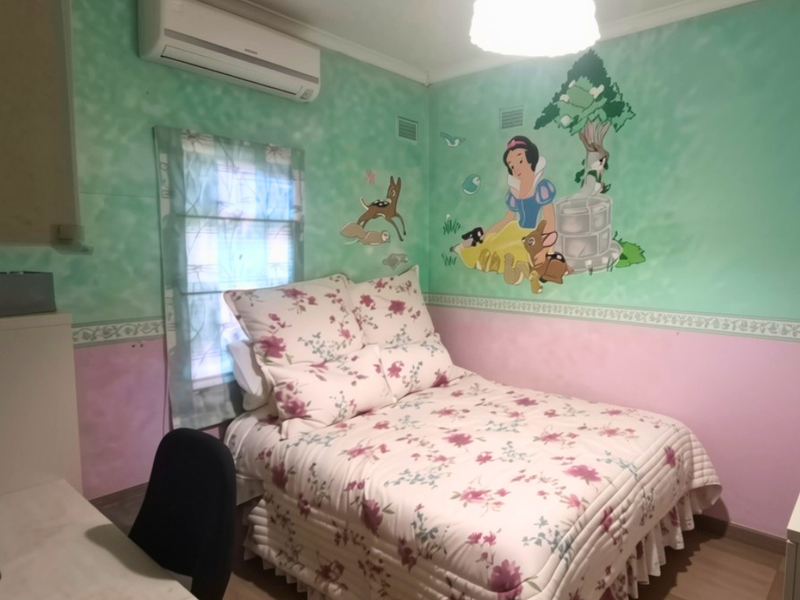 A bedroom featuring a split-system air conditioner, laminate flooring, and decorative wall murals, currently requiring cosmetic updates to the wall finishes.