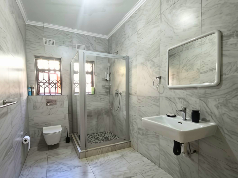 Modern bathroom featuring floor-to-ceiling marble-look tiling, a wall-mounted basin, a glass shower enclosure, and a wall-mounted toilet.