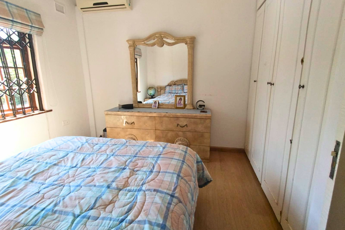 A bedroom featuring laminate flooring, built-in cupboards, and a wall-mounted air conditioning unit.