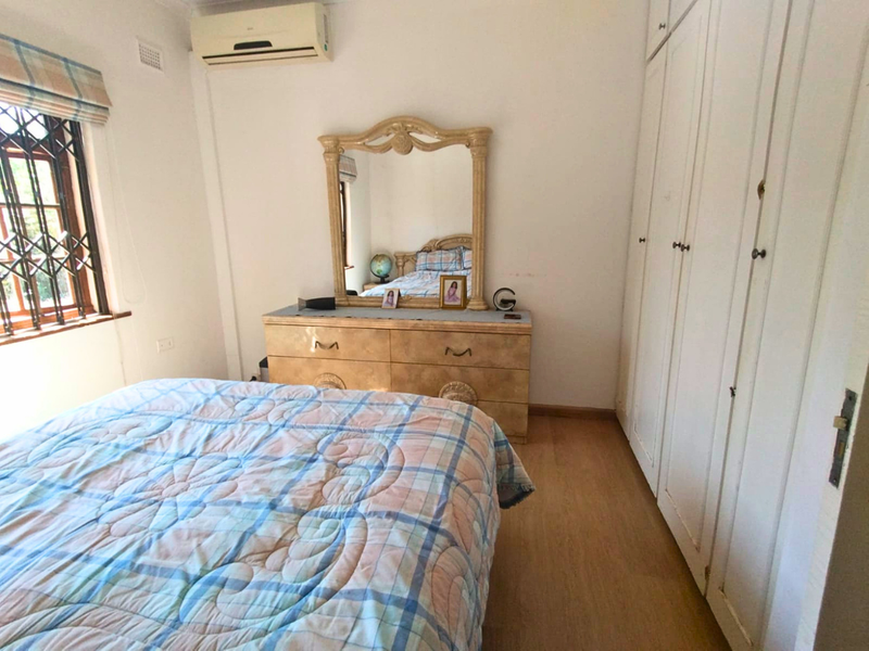 A bedroom featuring laminate flooring, built-in cupboards, and a wall-mounted air conditioning unit.