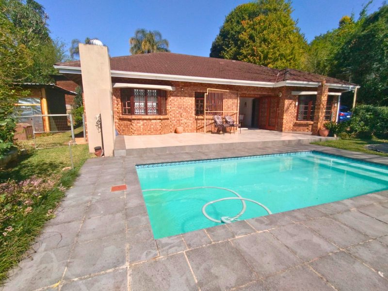 Rear view of a brick house featuring a swimming pool, paved patio area, and established garden surroundings.
