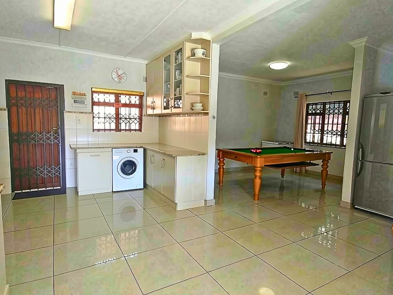 Open-plan living area featuring tiled flooring, built-in kitchen cabinetry, and security fixtures, seamlessly connecting the kitchen space to the adjacent recreational area.