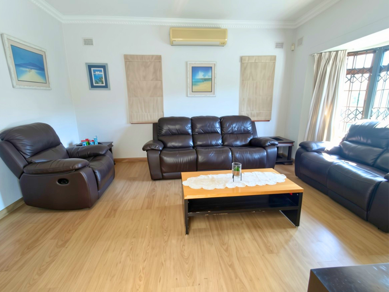 A well-lit living room featuring laminate flooring, crown molding, and a wall-mounted split-system air conditioning unit.