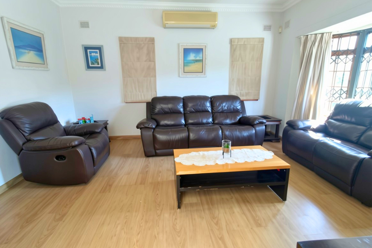 A well-lit living room featuring laminate flooring, crown molding, and a wall-mounted split-system air conditioning unit.