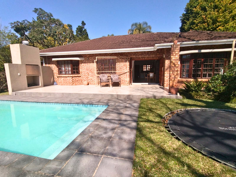 Rear view of a brick house featuring a swimming pool, tiled patio area, and a built-in outdoor braai facility.