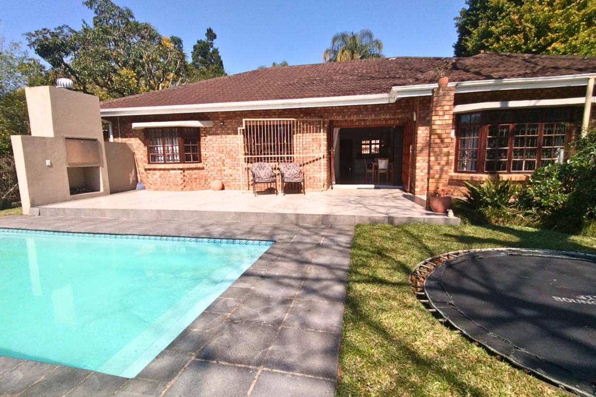 Rear view of a brick house featuring a swimming pool, tiled patio area, and a built-in outdoor braai facility.