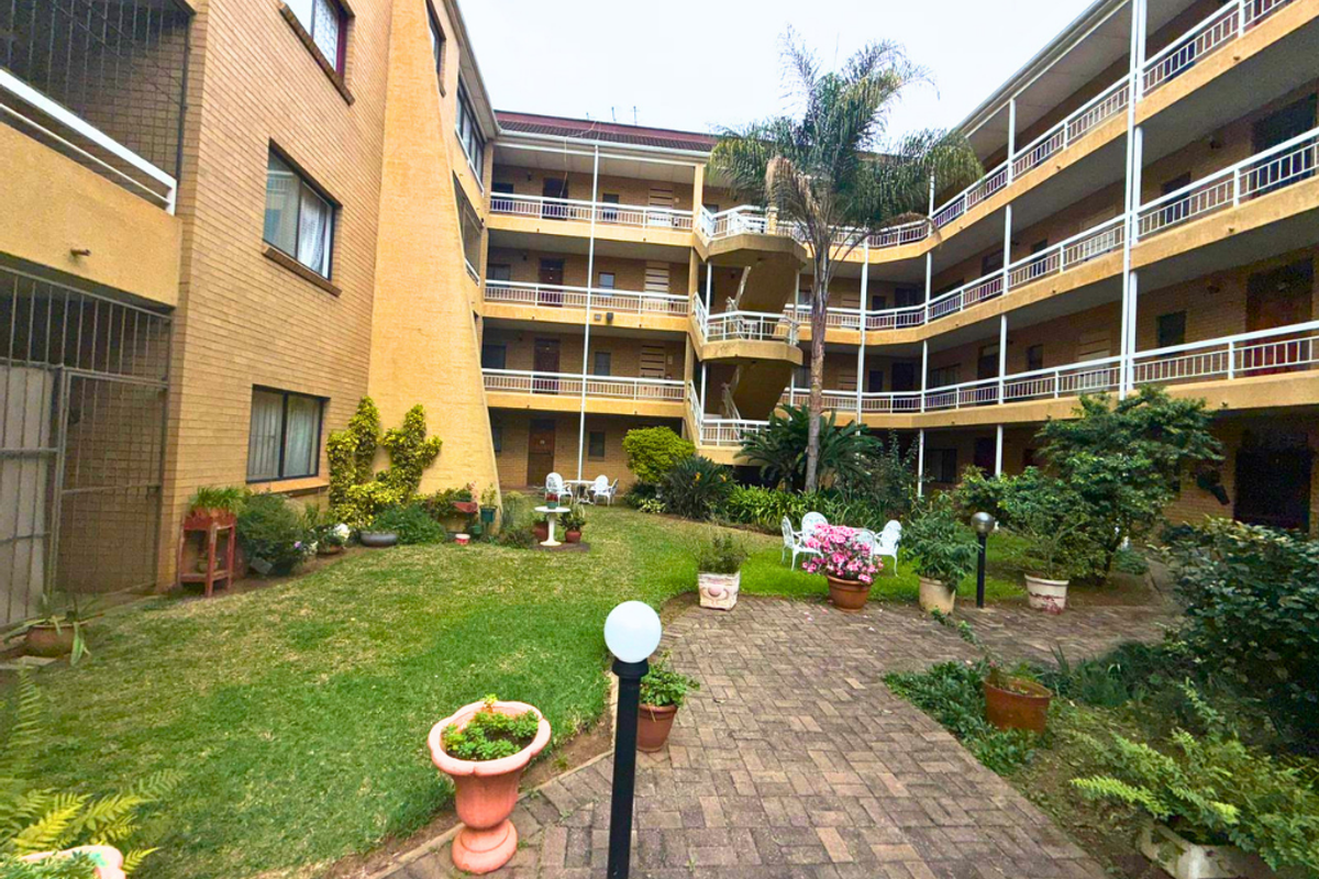 A view of the central courtyard and garden area of a multi-story apartment complex, featuring brick facades, tiered balconies, and a paved walkway.