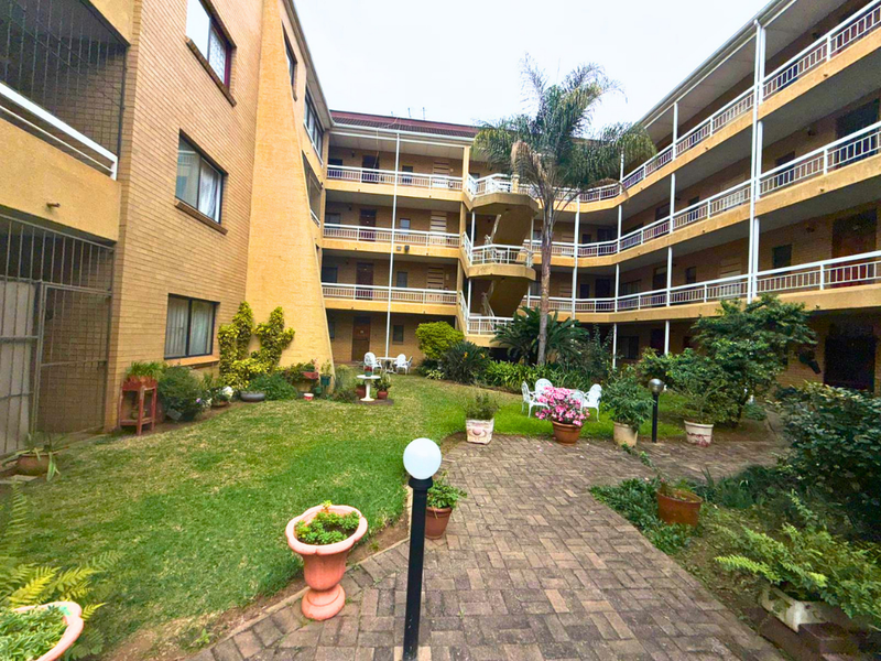 A view of the central courtyard and garden area of a multi-story apartment complex, featuring brick facades, tiered balconies, and a paved walkway.