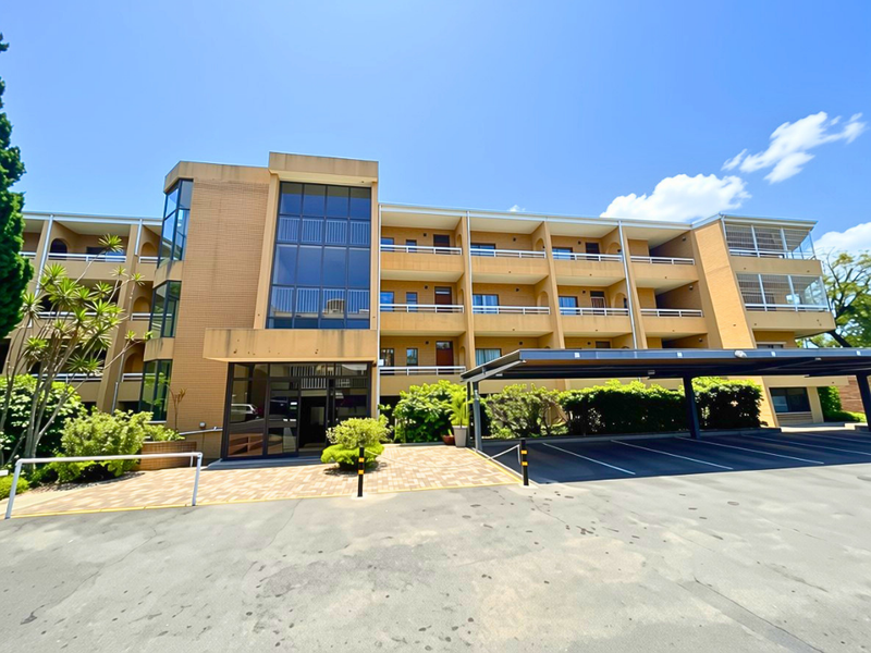 Front elevation of a multi-story apartment building featuring a brick facade, covered parking bays, and private balconies for each unit.