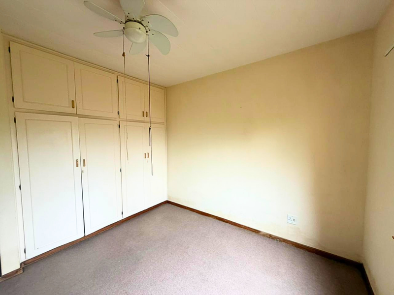 An empty bedroom featuring built-in cupboards, a ceiling fan, and carpeted flooring, presenting a blank canvas for potential updates and personalization.