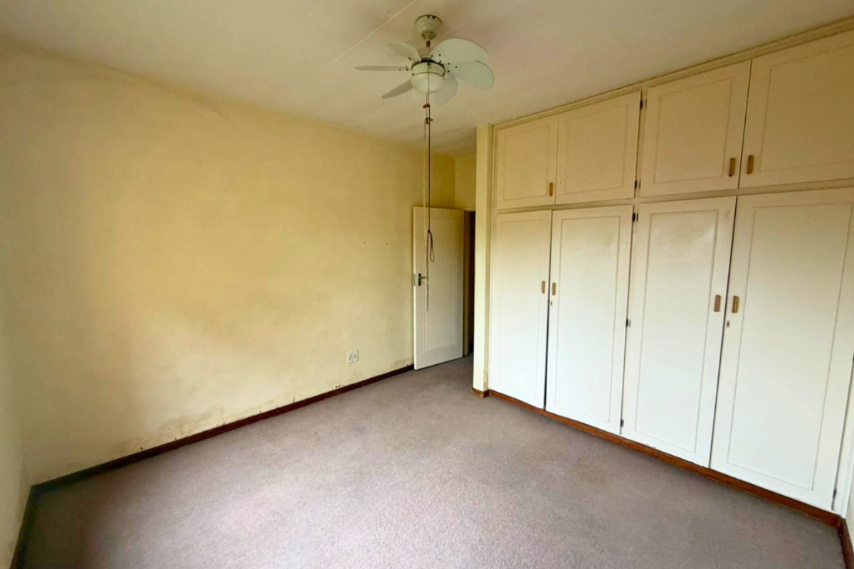 An empty bedroom featuring built-in cupboards, a ceiling fan, and carpeted flooring, requiring cosmetic updates to the walls.