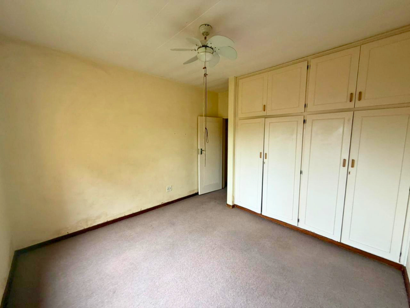 An empty bedroom featuring built-in cupboards, a ceiling fan, and carpeted flooring, requiring cosmetic updates to the walls.