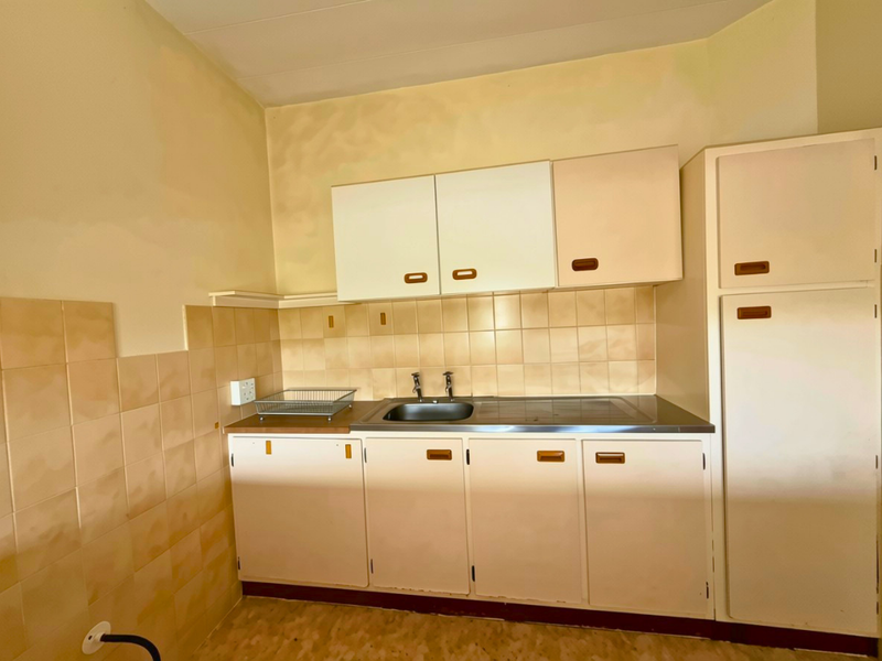 A compact, dated kitchen featuring original built-in cabinetry, a stainless steel sink, and tiled splashbacks, offering significant potential for modernization.