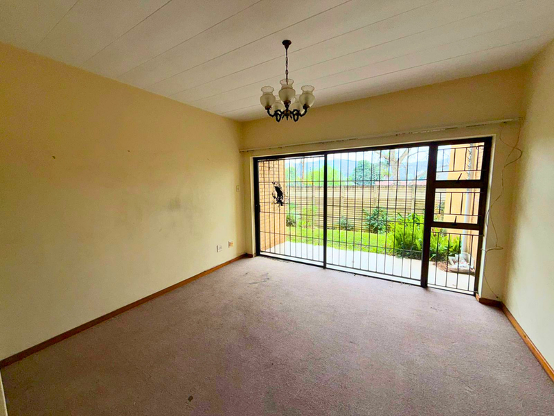 An empty living room featuring carpet flooring, a ceiling light fixture, and a large sliding glass door with an integrated security gate leading outdoors.