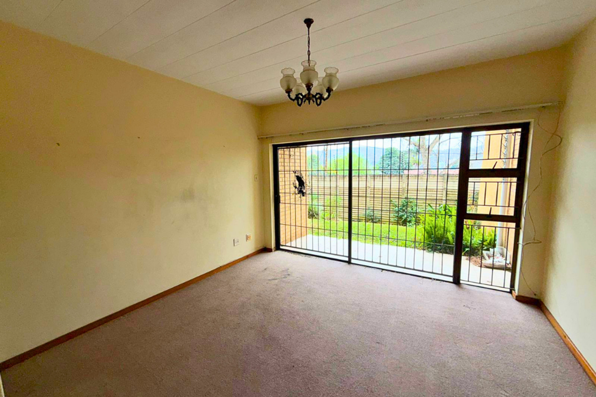 An empty living room featuring carpet flooring, a ceiling light fixture, and a large sliding glass door with an integrated security gate leading outdoors.